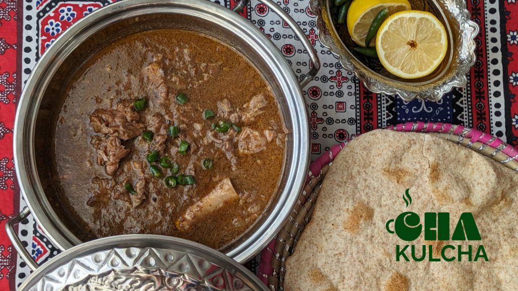 To the left is a metal serving bowl filled with Nihari, in the upper right is a smaller dish consisting on lemons and chilis, lower right is some flatbread